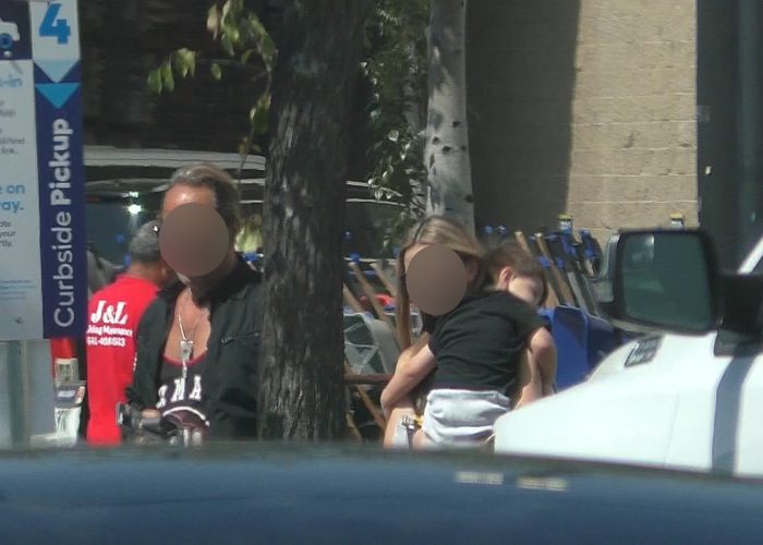 Adult holding a child beside another adult outside a store during surveillance.