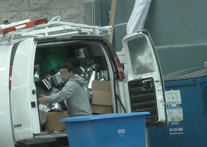 Person handling metal ductwork beside a work van during surveillance.